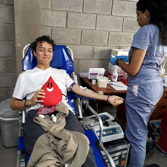 Un chico donando sangre y sosteniendo un peluche de personaje de gotita de sangre.
